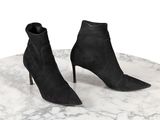 des bottines noires en daim posées sur une table en marbre, sur fond blanc
