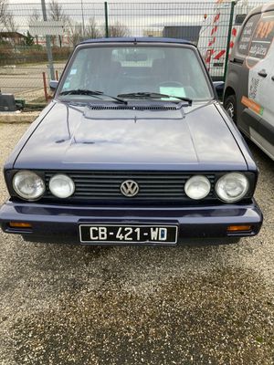 une Volkswagen Golf bleue garée sur un parking à côté d'une camionnette