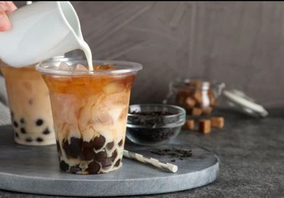 une personne en train de verser du lait dans un verre de thé aux perles
