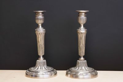 pair of silver candlesticks on a table against a black background