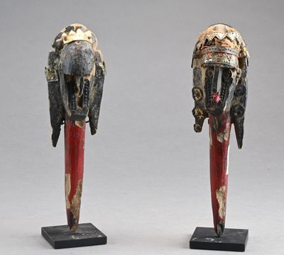 une paire de masques en bois sculptés posés sur des socles, sur une surface grise