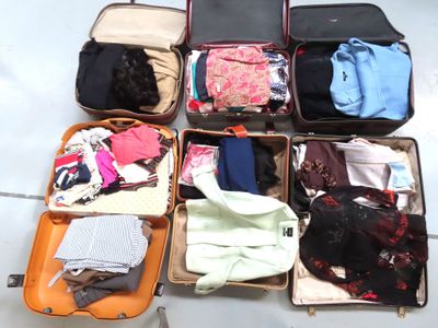 plusieurs valises ouvertes, contenant des vêtements, posées par terre