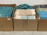 trois cartons remplis de t-shirts de différentes couleurs posés sur un sol carrelé