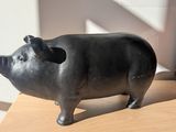 statue d'un cochon assis sur une table en bois, à côté d'un sac rouge