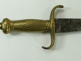a gold colored sword with a black handle on a white surface