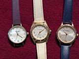 three different colored watches are lined up on a red surface