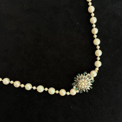 a necklace with pearls and a flower on a black background
