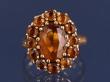 une image représentant une bague ornée d'une grosse pierre orange entourée de petites boules en or