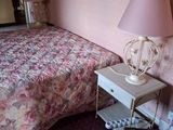 un lit recouvert d'une couette à motifs floraux, à côté d'une table de chevet sur laquelle est posée une lampe