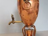 a large copper coffee pot on a stand with a faucet