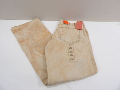 un pantalon beige, avec une étiquette à l'arrière, posé sur une surface blanche