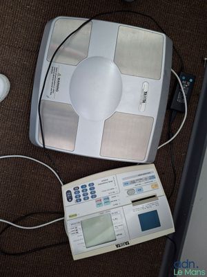 une balance électronique blanche posée par terre à côté d'une souris