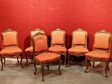 Six chaises anciennes sont alignées contre un mur rouge dans une pièce