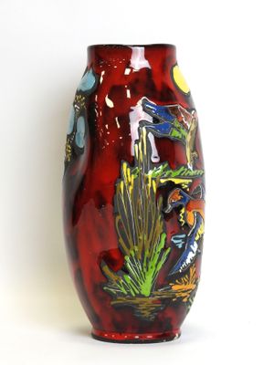 a red vase with birds on it on a white surface