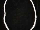 un collier de perles blanches avec un fermoir en or sur fond noir