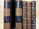 Plusieurs vieux livres sont alignés sur une étagère posée sur un support en bois.