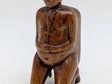wooden figurine of a man sitting on a stool with his hands on his stomach