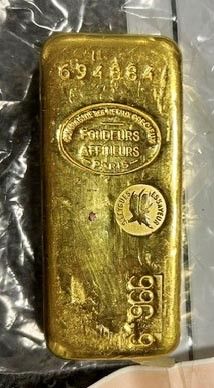 un lingot d'or posé sur un sac en plastique, à côté d'une main