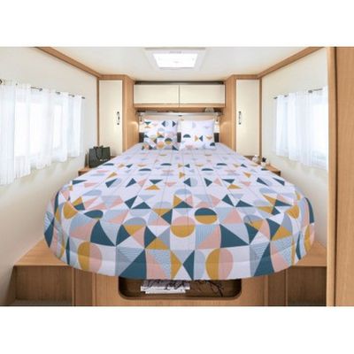 un lit au milieu de la pièce, recouvert d'une couette colorée