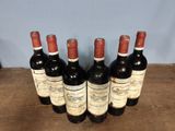 six bottles of red wine lined up on a wooden table