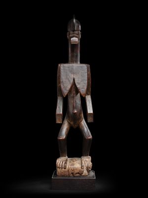 une statue en bois représentant un homme debout au sommet d'un rocher