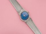 une image représentant une montre-bracelet au cadran bleu sur un fond rose