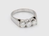 a close up of a three stone diamond ring on a white surface