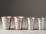 four silver cups with designs on them are lined up on a table