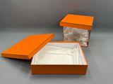 une boîte orange contenant un drap blanc, posée sur une surface grise