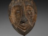 un gros plan d'un masque en bois posé sur un socle, sur une surface blanche