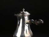 une cafetière ancienne en argent posée sur un support, sur fond noir