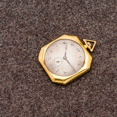 une petite montre de poche en or posée sur un tissu marron