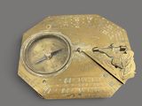 an antique brass compass on a gray surface with a clock