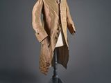 un vieux manteau posé sur un mannequin, devant un fond gris