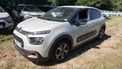 une petite voiture blanche garée dans un champ, avec d'autres voitures en arrière-plan