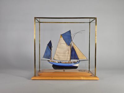 une petite maquette en bois représentant un voilier, exposée dans une vitrine