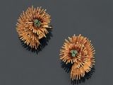 une paire de boucles d'oreilles en or et émeraude posées sur un fond noir