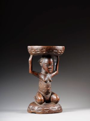 une statue en bois représentant une femme tenant un bol sur la tête