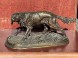 statue en bronze représentant un chien, posée sur un socle en bois avec un fond rouge
