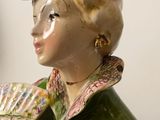 a figurine of a woman holding a fan and a bird on top of her head