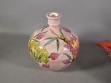 a pink vase with a bird on it next to a basket of flowers
