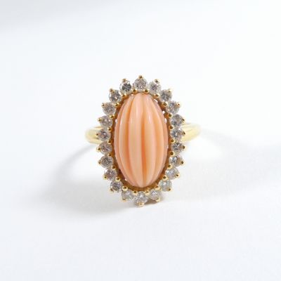 une photo d'une bague ovale en corail et diamants posée sur une surface blanche