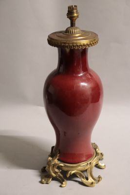 un vase rouge avec un couvercle doré posé sur une surface blanche