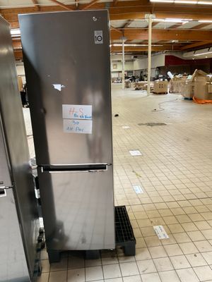 un réfrigérateur argenté posé dans un entrepôt, avec des cartons par terre