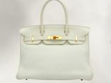 a white leather handbag with gold hardware on a white background