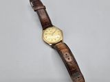 une montre en or avec un bracelet en cuir marron posée sur un fond blanc