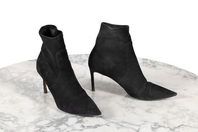 des bottines noires en daim posées sur une table en marbre, sur fond blanc