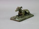 bronze statue of a dog laying on a rock on a white surface
