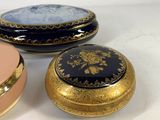 three small round boxes with gold trims and blue and pink designs on them