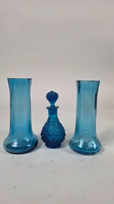 trois vases en verre bleu posés les uns à côté des autres sur une surface blanche